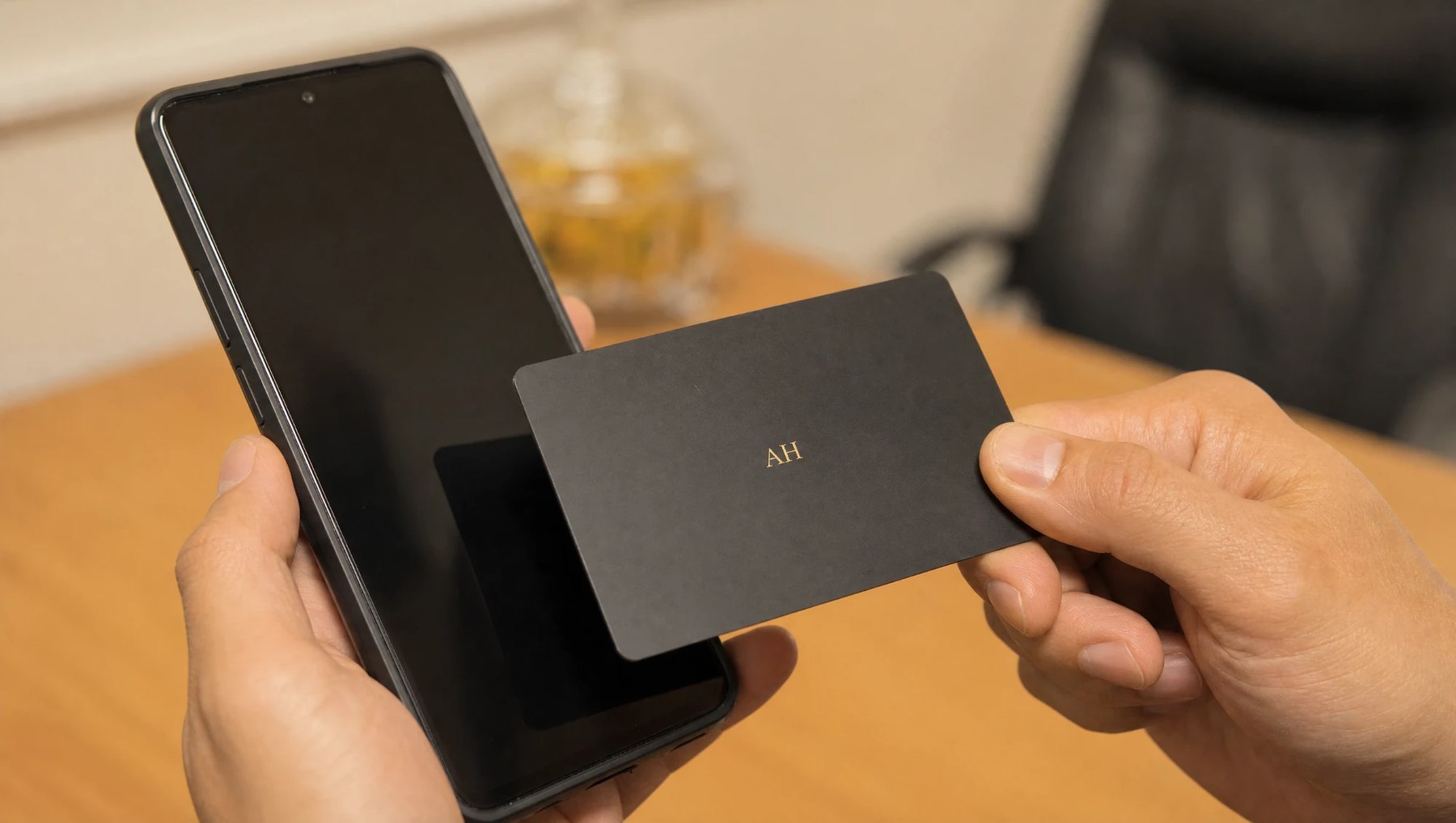 A black PVC contact card being tapped against a phone held in the other hand